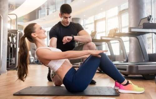 Kvinne som gjør mageøvelser med en personlig trener på et treningsstudio for å gjøre fremskritt i treningen.
